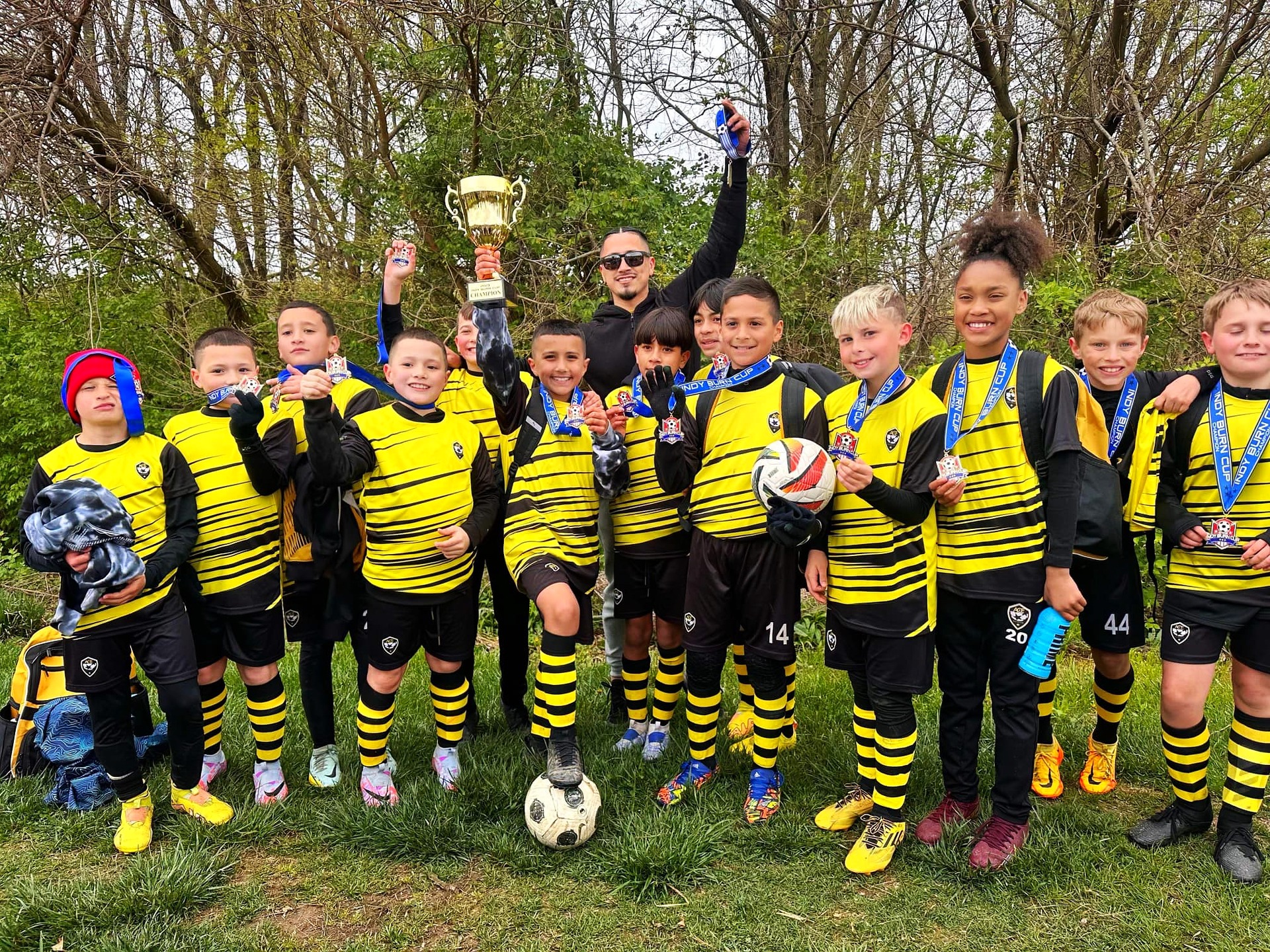ACE Boys team in striped kits celebrating with trophy at outdoor tournament